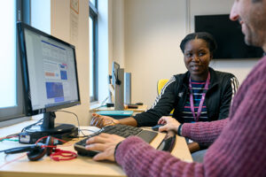 Two healthcare professionals collaborate at a desk, focused on a computer screen, engaged in a productive discussion.