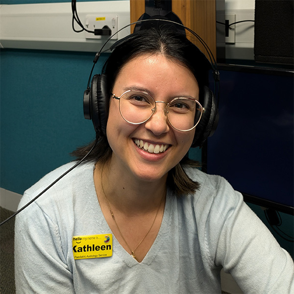 Image of Kathleen Sear, smiling on camera, with headphones on her