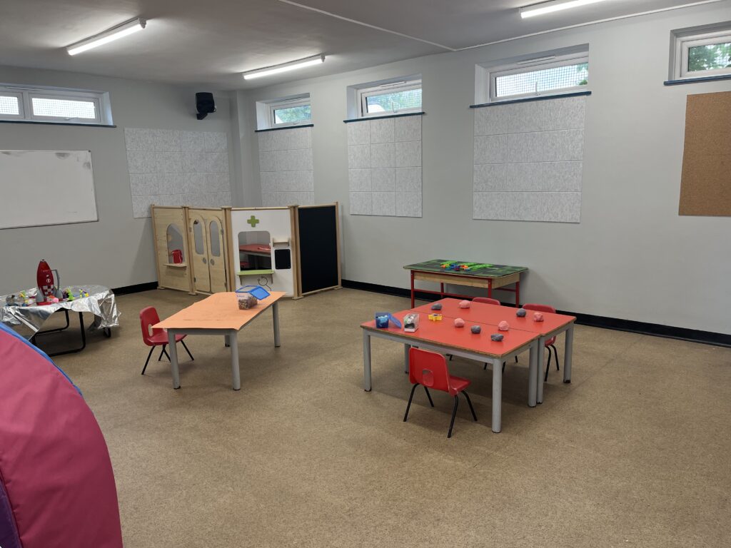 The play area in the children's centre: a room with three tables with chairs and various toys and learning materials on the tables.